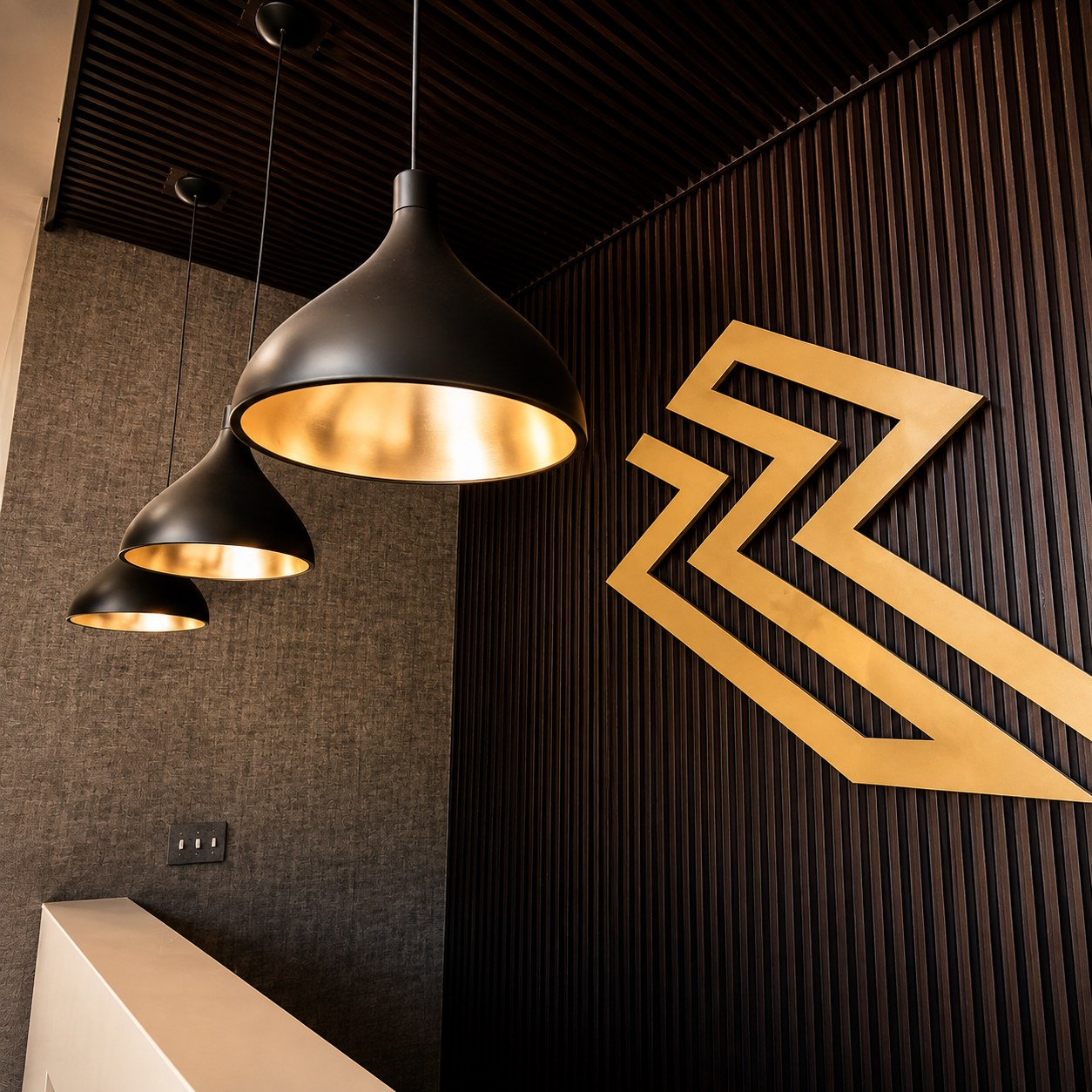 Black pendant lights and the brass Ramp N Rize logo in the Leetsdale lobby
